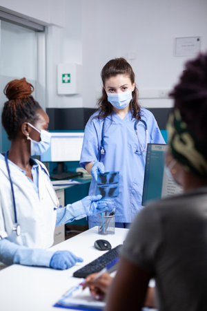 Doctor discussing x-ray ct scan patient diagnosis results and illness treatment plan with nurse during medical appointment. Hospital radiology medical exam wearing face mask and medical glovesの写真素材