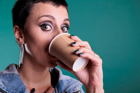 Confident satisfied woman holding cup of coffee enjoying hot beverage in front of camera, having work break in studio with isolated background. Cheerful model relaxing while drinking cappucinoの写真素材