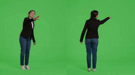 Office accountant advertising wave to call someone over, asking for person to come in studio. Female manager in suit raising hand standing over full body isolated greenscreen background.の写真素材