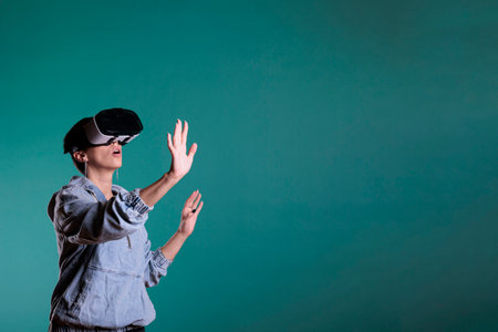 Smiling fun caucasian female wearing virtual reality headset with video interaction, standing over...