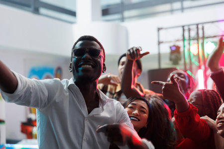 Cheerful happy friends taking selfie while partying together in nightclub. Diverse young carefree people looking at smartphone camera while making photo on club dancefloorの写真素材