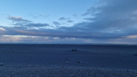 Icelandic beachfront setting at sunset with rosy sky and frosty pastures, black sand beach offering picturesque sight. Scenery around huge open water in icelandic environment.の写真素材