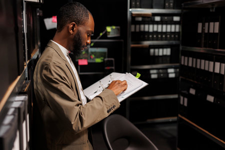 Investigator studying folder with police records in archive in office. African american detective...