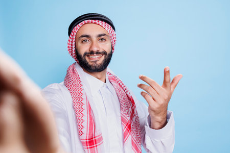 Cheerful muslim man wearing traditional clothes engaging in video call from pov perspective. Smiling...