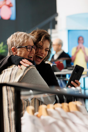 Playful women taking picture with smartphone, smiling at camera in clothing store. Cheerful clients shopping for formal wear, buying stylish clothes and fashionable merchandise in retail boutiqueの写真素材