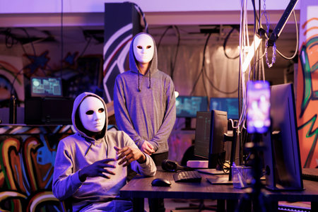 Scammers recording ransom message for victim to receive payment illegally. Anonymous hacker threatening on mobile phone camera while planning internet fraud in abandoned warehouseの写真素材