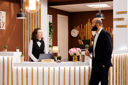 Businessman on work trip at hotel, talking to front desk staff about room services and check in process. Woman sharing information with important client, travelling for business meetings.の写真素材