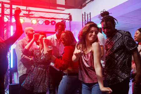 Passionate man and woman couple dancing together and moving to music beats in nightclub. African american boyfriend and caucasian girlfriend partying on dancefloor at discothequeの写真素材