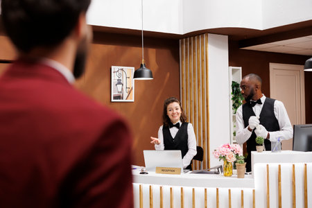 Receptionist greets hotel guest, providing excellent concierge services for businessman on work trip. Traveller with luggage being welcomed by front desk staff and bellboy, luxury resort.の写真素材