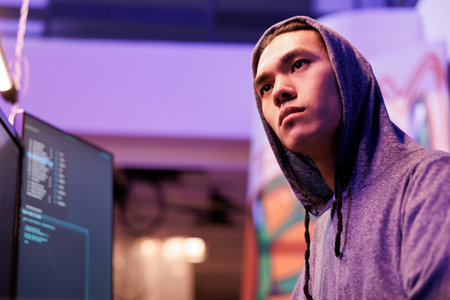Concentrated asian criminal coding malware on computer while breaking law. Young focused hacker in...