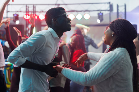 Carefree african american couple dancing together and having fun in nightclub. Cheerful young man and woman clubbers holding hands and partying on dancefloor while clubbingの写真素材