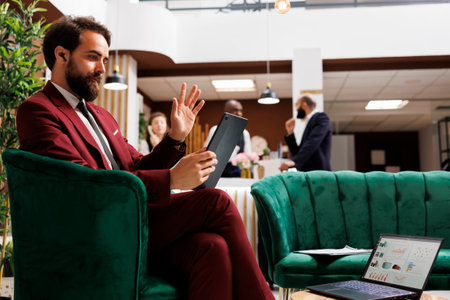 Company representative in lounge area using videocall connection on tablet to discuss about new collaboration. Employee on business trip meeting online with manager, teleconference concept.の写真素材