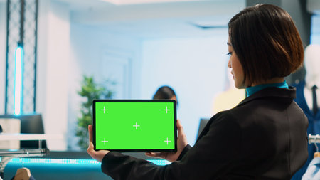 Female store assistant using tablet with greenscreen, working in clothing store. Young woman holding...