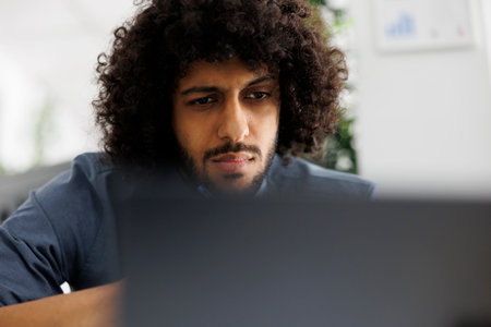 Focused arab entrepreneur working at financial data and analyzing report on laptop. Concentrated start up company man employee planning marketing strategy in business officeの写真素材