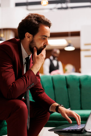 Businessman travelling on work trip and reviewing company notes to present at official conference internationally. White collar worker using laptop in hotel lounge area, collaboration.の写真素材
