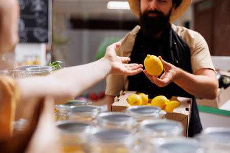 Customer in zero waste supermarket talking with shopkeeper, inquiring about freshly received batch of farm grown organic fruits. Environmentally mindful client in eco store asking for healthy productsの写真素材
