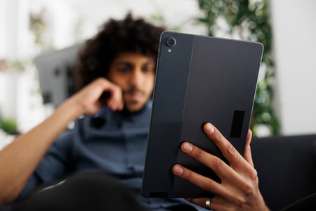 Young arab entrepreneur reading article on digital tablet while working in business office. Start up...