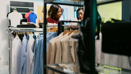 Young people talking about fashion collection in store, customer and employee looking at trendy new clothes in boutique. Two women analyzing retail shop merchandise at shopping center.の写真素材