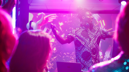 Male DJ using audio mixing station at party, putting modern music for crowd of people on dance...