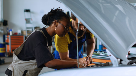 Coworking technicians in car service using torque wrench to fix damaged automobile. Man and woman in repair shop servicing broken vehicle, checking for faulty transmission using professional toolsの写真素材