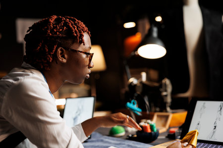 Close up of african american couturier wearing glasses looking online for fashion design...