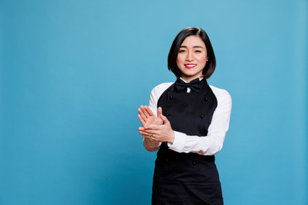 Cheerful asian waitress applauding and looking at camera with happy expression. Smiling joyful woman...
