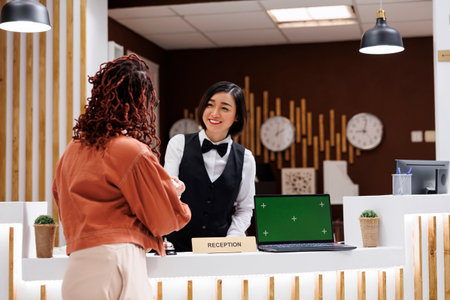 Hotel staff giving access key card to guest, having laptop with greenscreen template on reception counter. Employee working at front desk with chroma key display and isolated mockup.の写真素材