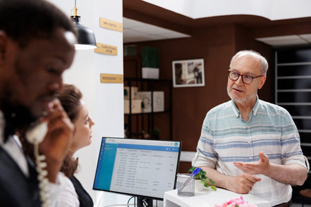 Kind female concierge at hotel lobby welcomes elderly man and helps him check in. Senior male traveler at luxury resort asks caucasian receptionist for recommendations on finest holiday activities.の写真素材