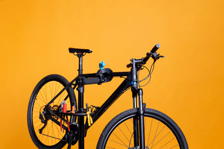 View of bicycle on repair-stand surrounded by specialized equipment outside for maintenance and repair. Modern damaged bike for repairing and adjusting, positioned in front of yellow background.の写真素材