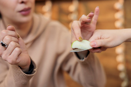 Young woman customer tasting fresh organic green apple while shopping at outdoor farmers market, selective focus. Female customer sampling locally grown organic fruits before purchaseの写真素材