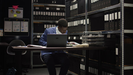 African american private investigator conducting a discreet investigation and analyzing evidence. Detail-oriented male law officer investigates case files and clues to combat organized crime.の写真素材