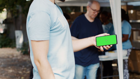 Detailed view of person horizontally holding mobile phone at charitable food drive, presenting an...
