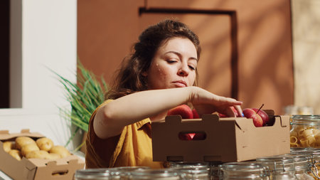 Vegan woman in sustainable zero waste supermarket smelling apples before adding them to shopping basket. Client in local neighborhood grocery shop picking locally grown fruitsの写真素材