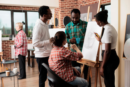 Young people friends taking drawing class in art studio, attending creative workshop together. Group of African American students men and women listening to teacher, learning sketching techniquesの写真素材