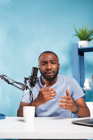 African american blogger speaking in microphone while streaming online on web channel. Young man vlogger talking with subscribers while creating digital content and recording video portraitの写真素材