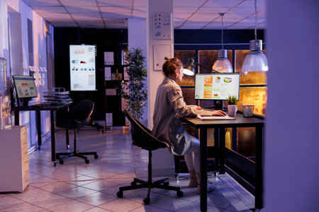 Businesswoman sitting at desk table in startup office working overtime at management project. Corporate worker planning financial investment strategy to increase company profit. Business conceptの写真素材