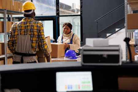 Woman package handler putting cardboard box on table and preparing parcel before shipment in warehouse. Deliver service african american worker packing carton in storage roomの写真素材