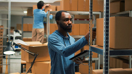 Male entrepreneur scanning storage room produucts with gadget and scanner, working on logistics and inventory. Young adult planning quality control management, checking packages.の写真素材