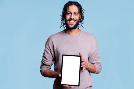 Smiling arab man showing digital tablet with white empty screen for application advertisement mock up. Happy person presenting portable gadget with blank touchscreen for product promotionの写真素材