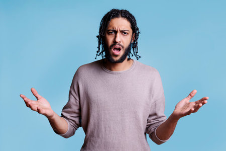 Angry arab man with open arms and confused facial expression portrait. Young attractive dissatisfied person with negative emotion shouting and looking at camera while posing for studio shotの写真素材