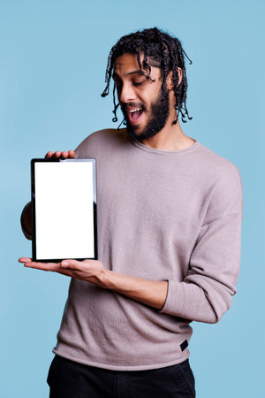 Cheerful arab man holding digital tablet and looking at white blank screen for product marketing mock up. Handsome model presenting device with empty display for promotional textの写真素材