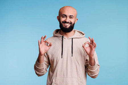 Smiling arab man showing ok gesture with two hands and looking at camera. Cheerful arabian bearded person posing with okay and agreement sign with fingers studio portraitの写真素材