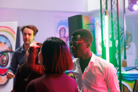 Young people partying at nightclub discotheque, celebrating and enjoying nightlife entertainment. Men and women clubbing, dancing and moving to techno music rhythm on dancefloorの写真素材