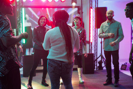 People laughing and dancing together while partying in nightclub. Diverse clubbers crowd enjoying...
