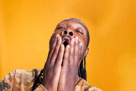 Portrait of exhausted african american person covering mouth with hand being tired while posing in...
