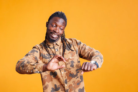 African american businessman hurrying up at job, checking time on wristwatch in studio over yellow background. Executive manager running late and looking at clock, waiting for someoneの写真素材