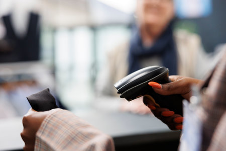 African american worker scanning fashionable shirt using store scanner, preparing purchase for elderly shopaholic woman. Client buying casual wear in clothing store, commercial activity. Close upの写真素材