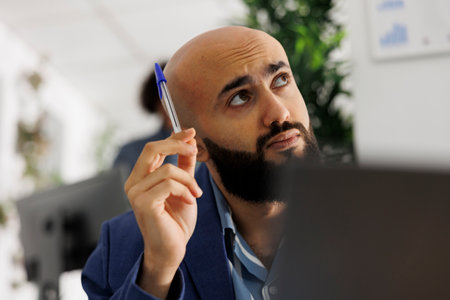Arab entrepreneur thinking and looking away while analyzing sales strategy on laptop. Young company employee managing financial data while working in start up business officeの写真素材