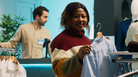 Female client looking at clothes on hangers and racks, examining merchandise in clothing store. Young woman buying fashionable casual wear on discount, commercial activity in shopping center.の写真素材