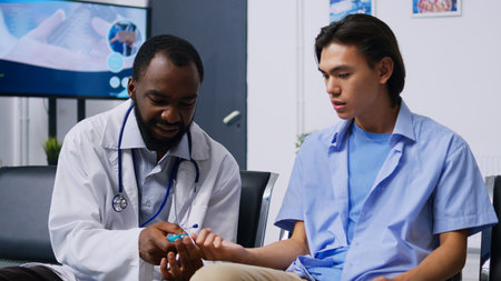 Specialist consulting asian patient with glucometer, measuring insulin and glucose level from blood sample. Doctor and young adult doing diabetic control during checkup visit in hospital reception.の写真素材